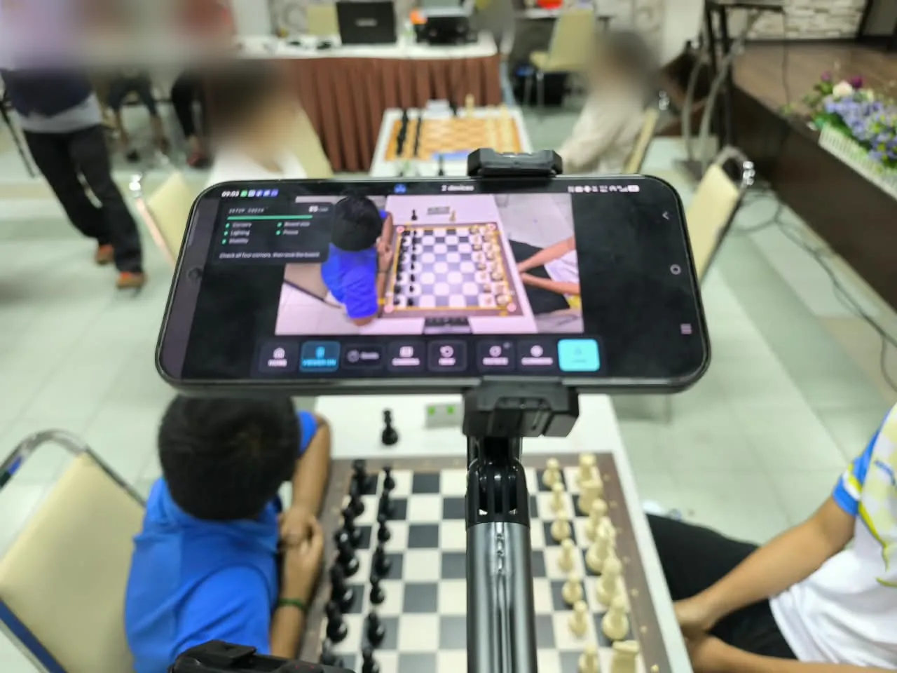 Camera phone on its stand at a tournament with the ChessZCam setup check panel; faces are blurred